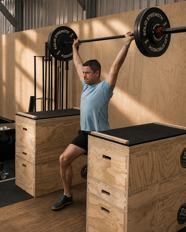 Close-up coaching moment, a strength coach adjusting an athlete's grip on a barbell during a one-on-one session, focused expressions, industrial gym background softly blurred, warm natural light, editorial photography