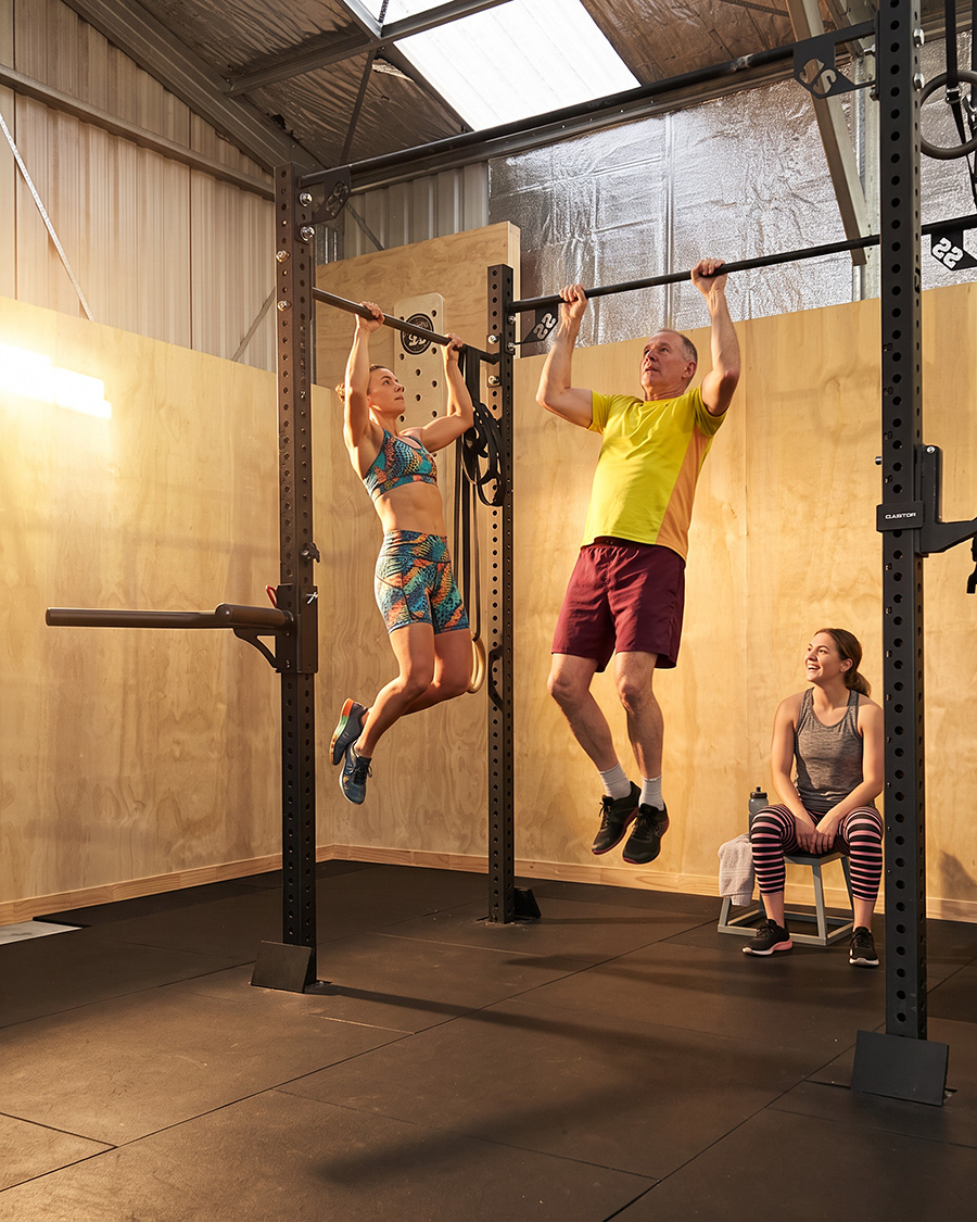 Vertical shot of a small group training together in an industrial gym, coach guiding the session in the foreground with two or three participants working behind, lifting platform and equipment visible, sense of camaraderie and effort, warm natural light, editorial fitness photography, portrait orientation